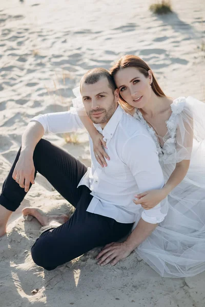Joven hermosa pareja abrazando y sentado en la playa de arena - foto de stock