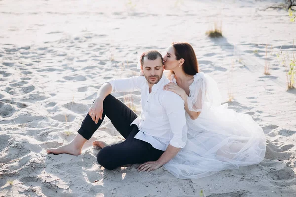 Beautiful woman kissing her boyfriend while sitting on beach — Stock Photo