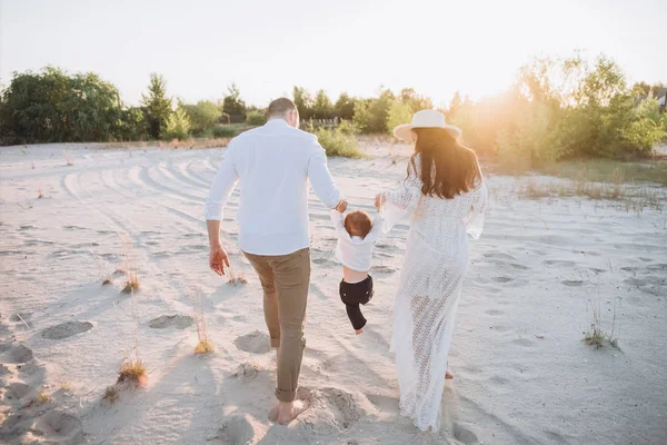 Задний вид семьи, держащейся за руки с ребенком на пляже с задним освещением — стоковое фото