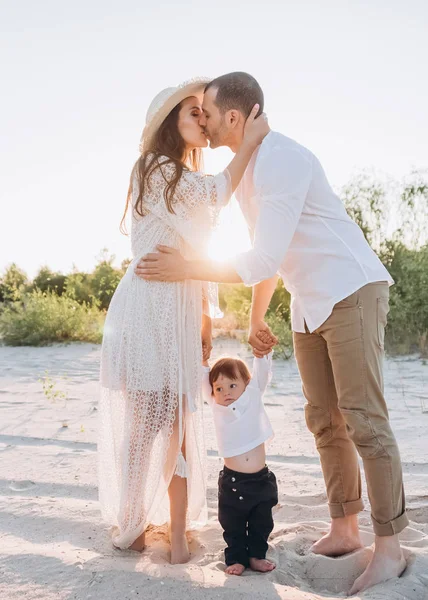 Madre y padre tomados de la mano con su hijo y besándose juntos - foto de stock