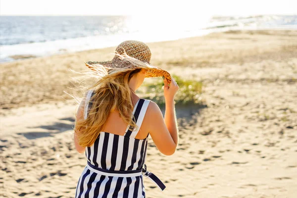 Vista trasera de la mujer en sombrero de paja caminando en la playa de arena - foto de stock