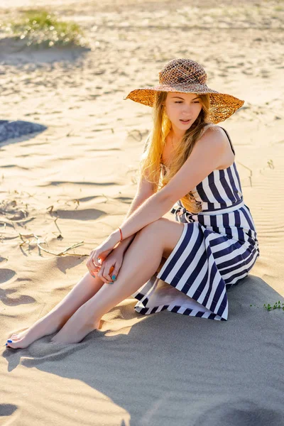 Beautiful pensive woman in striped dress sitting on sandy beach — Stock Photo