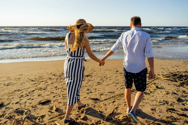 Visão traseira do casal afetuoso de mãos dadas e andando na praia de areia no dia de verão — Fotografia de Stock