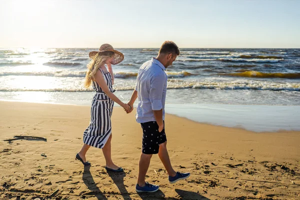 Vista lateral do jovem casal apaixonado de mãos dadas enquanto caminhava na praia de areia em Riga, Letónia — Fotografia de Stock