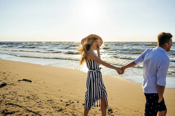 Side view of young smiling couple in love holding hands on sandy beach in Riga, Latvia — Stock Photo