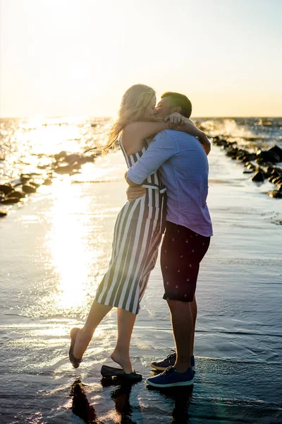 Beau couple amoureux étreignant et embrassant sur le bord de la mer pendant le coucher du soleil à Riga, Lettonie — Photo de stock