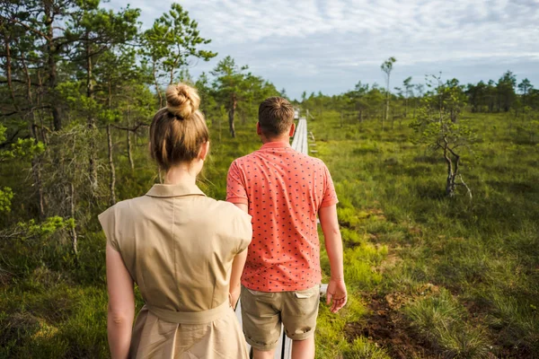 Vista trasera de pareja enamorada caminando sobre puente de madera con plantas verdes y cielo azul sobre fondo - foto de stock