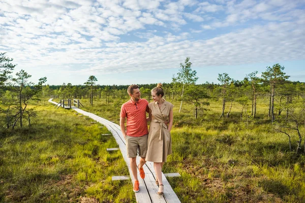 Coppia sorridente innamorata che cammina su un ponte di legno con piante verdi e cielo blu sullo sfondo — Foto stock