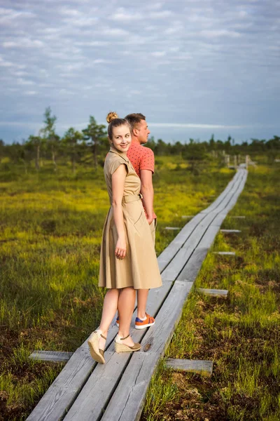 Young couple in love holding hands on wooden bridge with green plants on background — Stock Photo