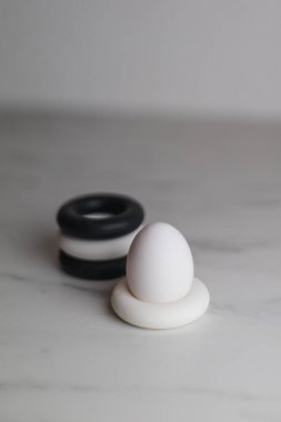 four black and white silicon eggcups on a marble table with only one egg, kitchen clipart