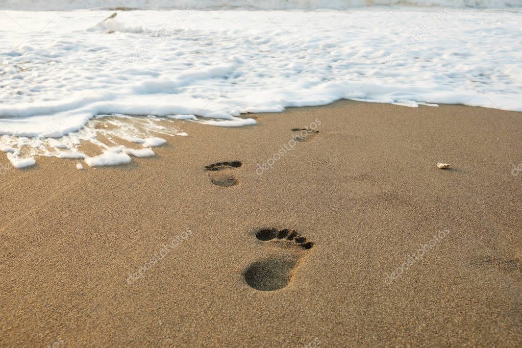 Footsteps in the sand to the foamy wave