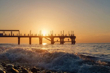 Çift dalgalar sıçramasına arkasında gün batımında iskelede silüeti