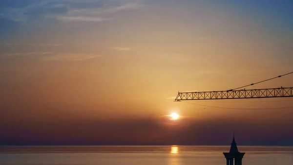 Detail of the construction crane against the cloudy sunset sky over the sea