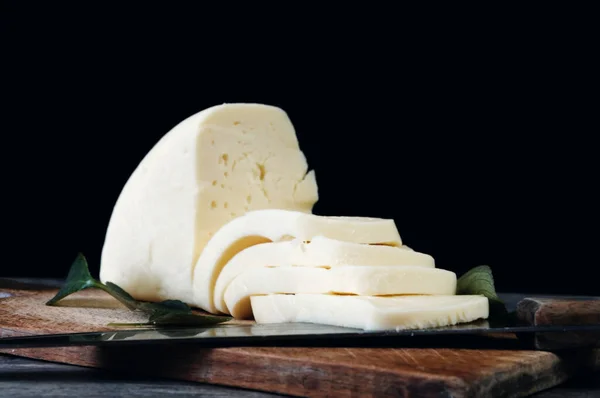 黒を背景に古い板の上にチーズをスライス グルジアチーズスルグニ — ストック写真