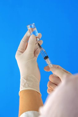 Beyaz eldivenli tıbbi personelin elinde şırınga ve ilaç şişesinden aşı var.