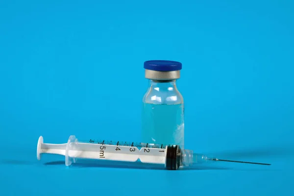 Medicine bottle for injection and a syringe on the blue surface