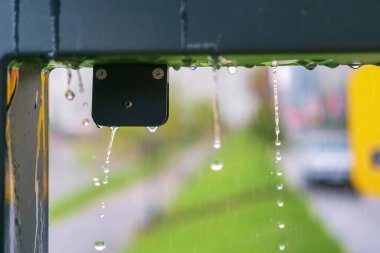 Bulanık, yağmurlu arka plan ve hareket halindeki su damlaları. Metal inşaattan sağanak yağmur yağıyor, seçici odaklanma