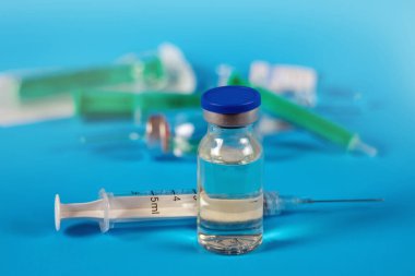 Enjeksiyon için ilaç şişesi mavi arka planda şırınga ve arka planda aşılar için bulanık ilaç şişeleri.