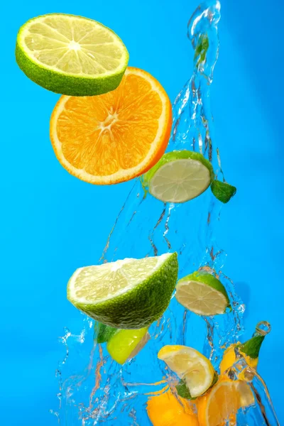 Falling fresh slices of the lemon and green mint leaves with fresh water in the air. Flying fruits concept on blue background