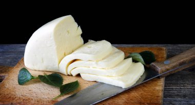 Siyah arka planlı eski tahta üzerinde dilimlenmiş peynir. Gürcistan peyniri sulguni