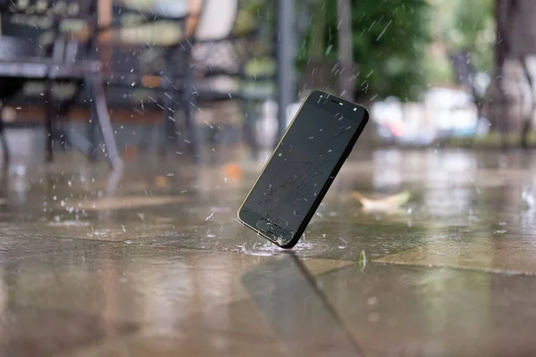 Akıllı telefonlu bir kaza. Yağmurlu bir günde şehir parkındaki ıslak zemine akıllı telefon düşüşü ve çarpışması seçici bir odak noktasıdır.