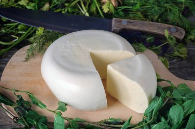 Ahşap bir tahtanın üzerinde yeşil otlarla kaplı bir peynir. Gürcistan peyniri sulguni üst görünüm