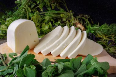 Tahtada dilimlenmiş peynir ve yeşil otlar. Gürcistan peyniri sulguni