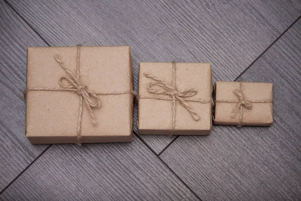 Present wrapped in craft paper with sack rope on wooden background. Smaller or bigger concept.