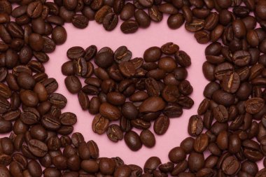 Coffee beans in heart shape on pink background.