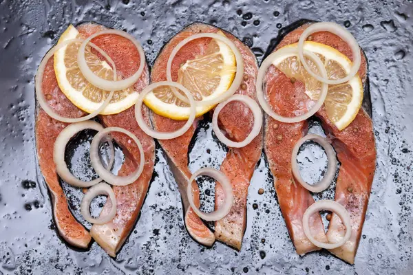 Kırmızı balık biftek (somon veya alabalık) siyah arka plan üzerine limon, tuz, otlar ile.