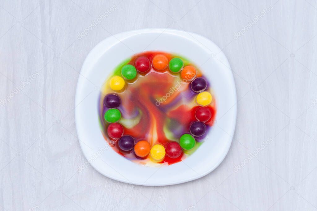 Science experiment for kids. Circle of colored candies on white plate.