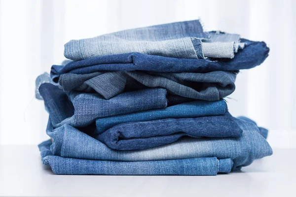 Stack of old blue jeans for recycling on white background.