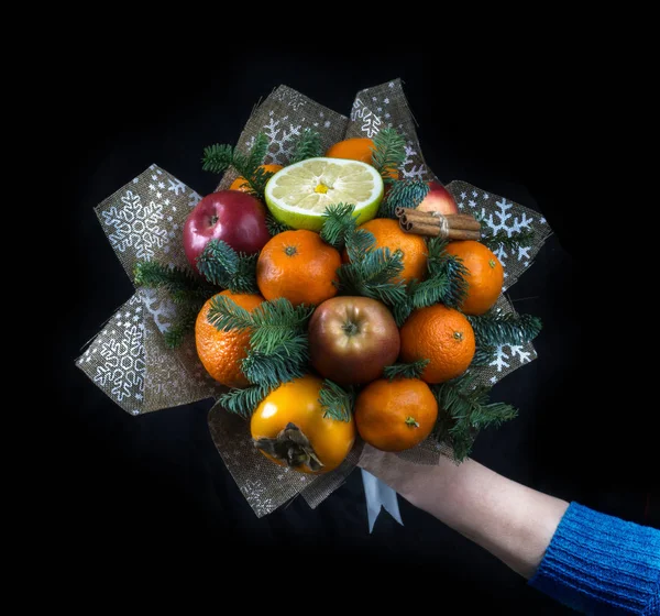 Meyve Birliğinde bir el. Bir Birliği'nde bir kırmızı elma, mandalina, Trabzon hurması, tarçın, oda işte. Köknar-ağaç dalları. Kare fotoğraf. Siyah bir arka plan üzerinde.