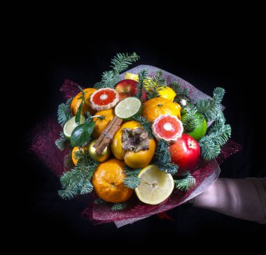Meyve Birliğinde bir el. Bir Birliği'nde bir kırmızı elma, mandalina, Trabzon hurması, tarçın, oda işte. Köknar-ağaç dalları. Kare fotoğraf. Siyah bir arka plan üzerinde. 