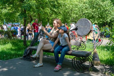 Anne ve kızı, parkta olağandışı bir bankta, sıradan bir bayramda selfie çekiyorlar.