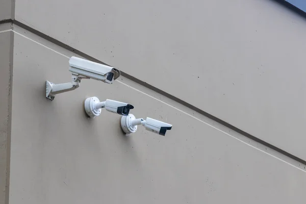 3 security cameras in a row on a light brown building wall