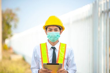 Asyalı mühendis yüz maskesi cep telefonu cihaz teknolojisi inşaat alanında çalışıyor.