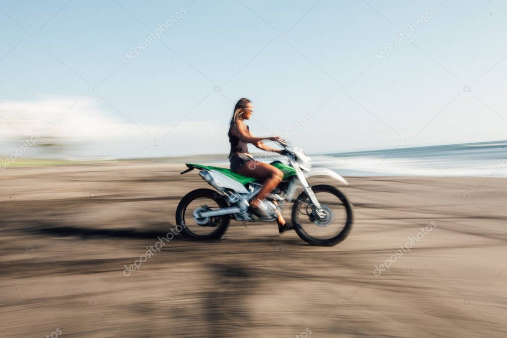 Motion blur image of Young afro american woman riding motorbike on the beach coastline