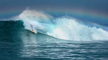 Surfer riding big green wave with rainbow in background in North Maluku islands, Indonesia clipart