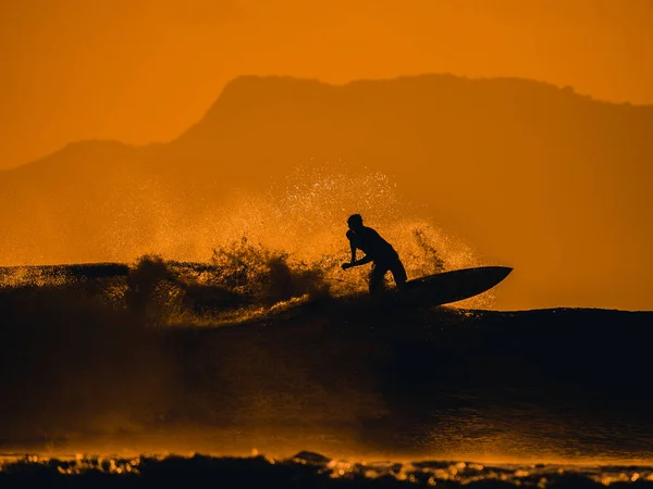 Silhouette of male surfer riding big ocean wave at orange sunset