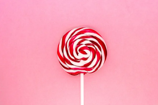 Round white and red lollipop with white stick on pink background surface
