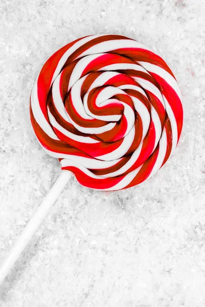 Round white and red lollipop with white stick on white artificial snow background surface