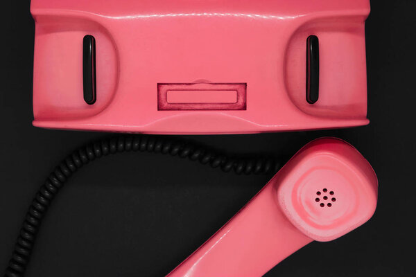 Top view of old and dirty pink retro telephone on black background surface