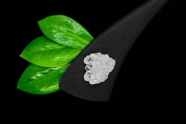 在黑色背景上分离的绿叶 黑色木制铲子和大糖或盐晶体的抽象成分 — 图库照片