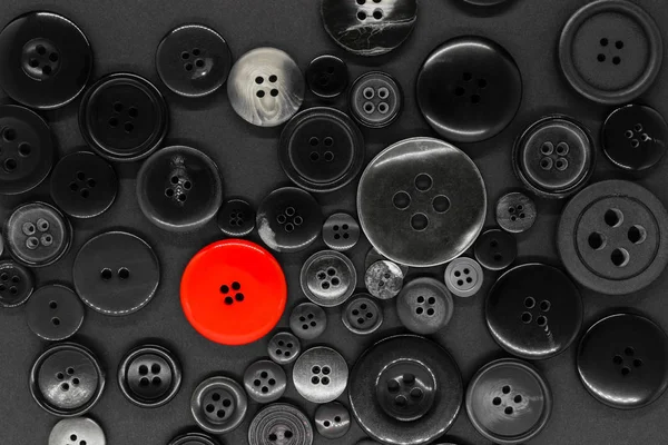 Various dark clothes buttons background with one red button