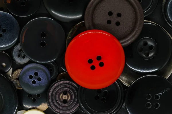 Various dark clothes buttons background with one red button