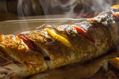 Kızarmış balık limon ve domates ile duman. Crisry kabuk ve duman yukarıdaki ile ızgara balık. Lezzetli pişmiş balık güneş ışığı altında. Pişmiş deniz ürünleri kavramı. Mutfak ve pişirme arka plan. Balık unu.