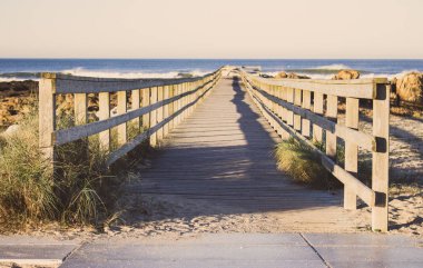 Ahşap iskele çim Atlantik Okyanusu kıyısında, Portekiz ile. Deniz kıyısında taşlarla için ahşap tahta yol. Şafakta dunes içinde boş geçit. Perspektif arka plan. Tropikal seyahat kavramı. Huzurlu doğal yer.