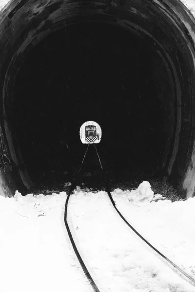 Railway tunnel with train at the end black and white. Locomotive at the end of tunnel monochrome. Transportation and road concept. Winter railroad travel. Rock vintage tunnel. Light at the end of tunnel.