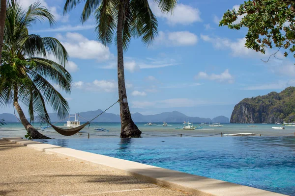 Pool and empty hammock with palm trees, isles and boats on background. Tropical beach. Philippines resort landscape. Idyllic vacation concept. Exotic travel concept. Palawan island. Tropics paradise.